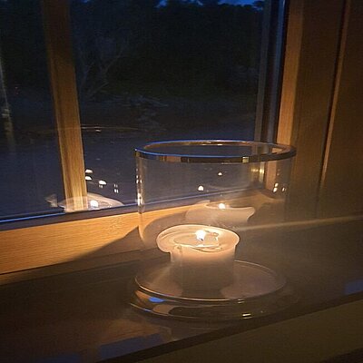 Foto: eine brennende Kerze eines Gemeindegliedes im Fenster